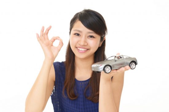 車の模型を片手にOKサインを出す女性