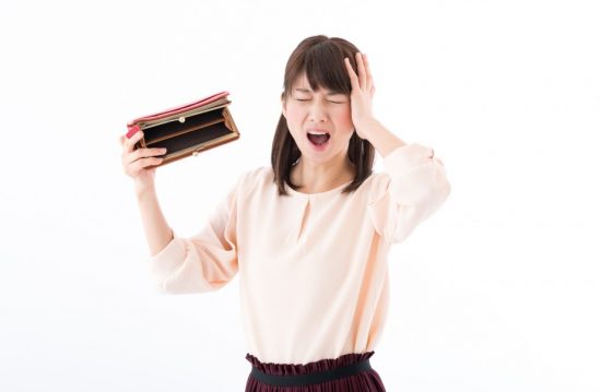 空っぽの財布に頭を抱える女性